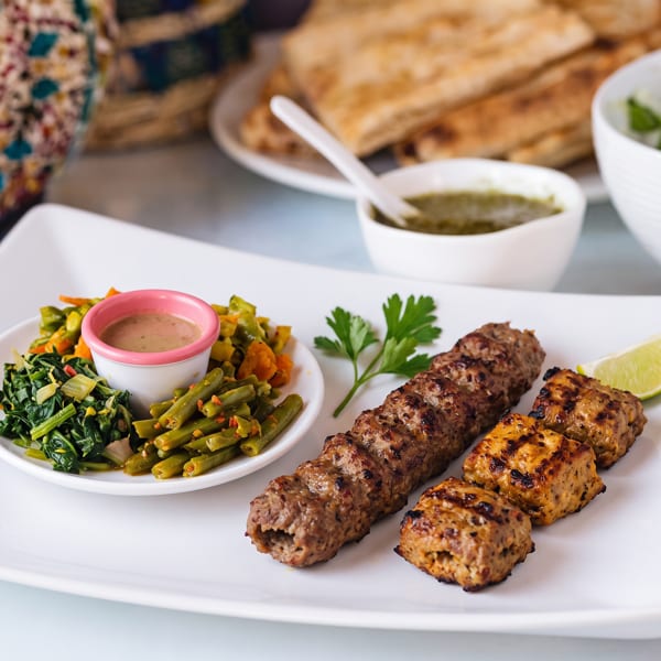 Grilled meat skewers, green beans, spinach, and dipping sauces on a white plate.