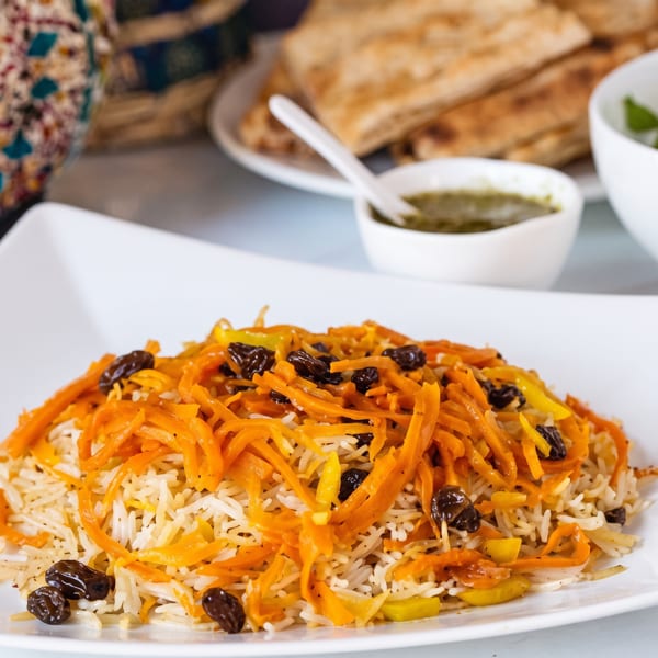 A close-up of a white plate filled with rice, shredded carrots, and raisins, with flatbread in the background.